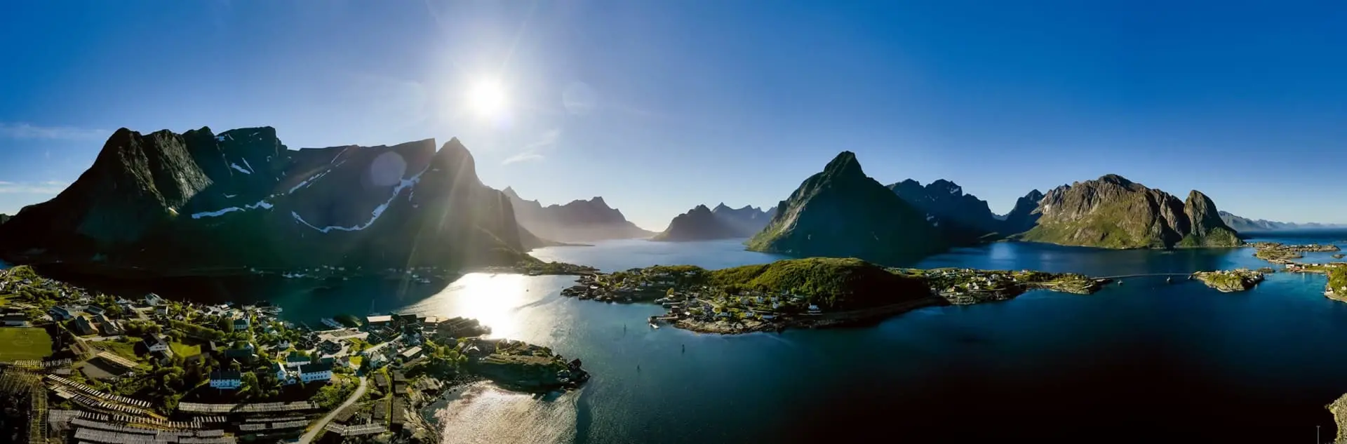Lõunapäikese valgustatud fjordi ja majadega kaljused mäed ning sinine vesi Norra maastikus.